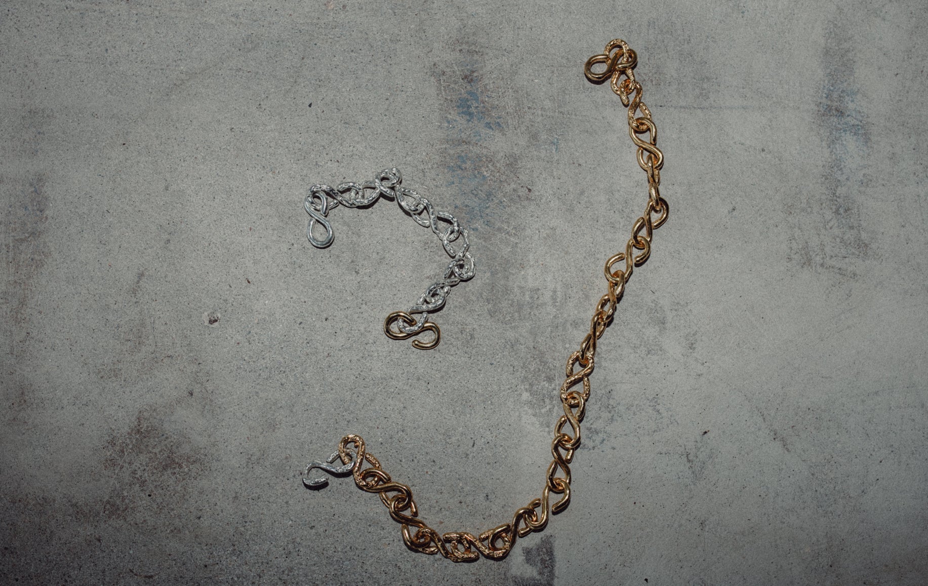 Gold layered necklaces featuring a chunky chain and a pendant with an organic textured finish, displayed on a model wearing a white outfit.