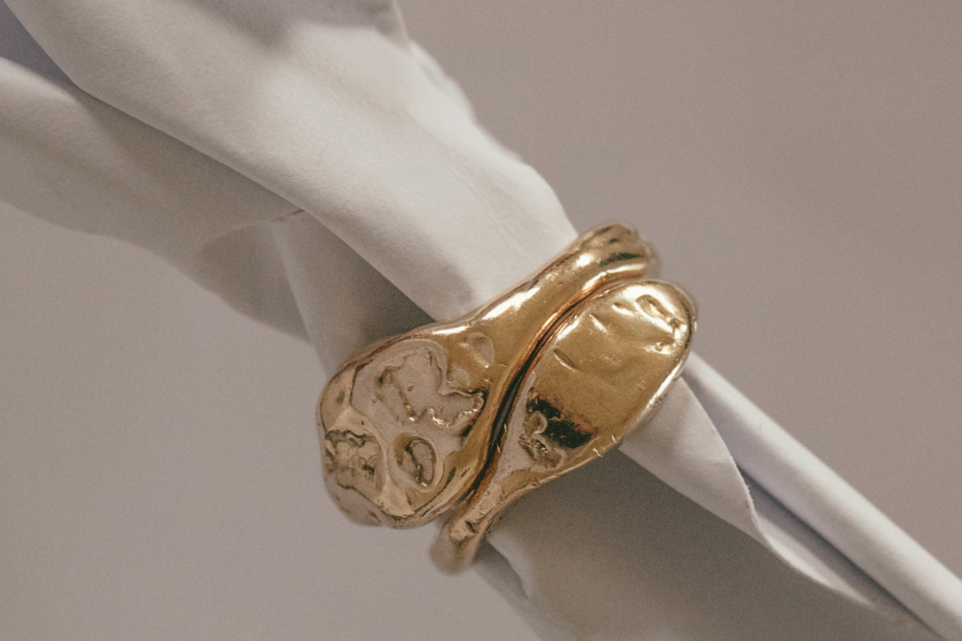 Gold wedding band with an organic, sculptural design, displayed elegantly on a soft white fabric background.