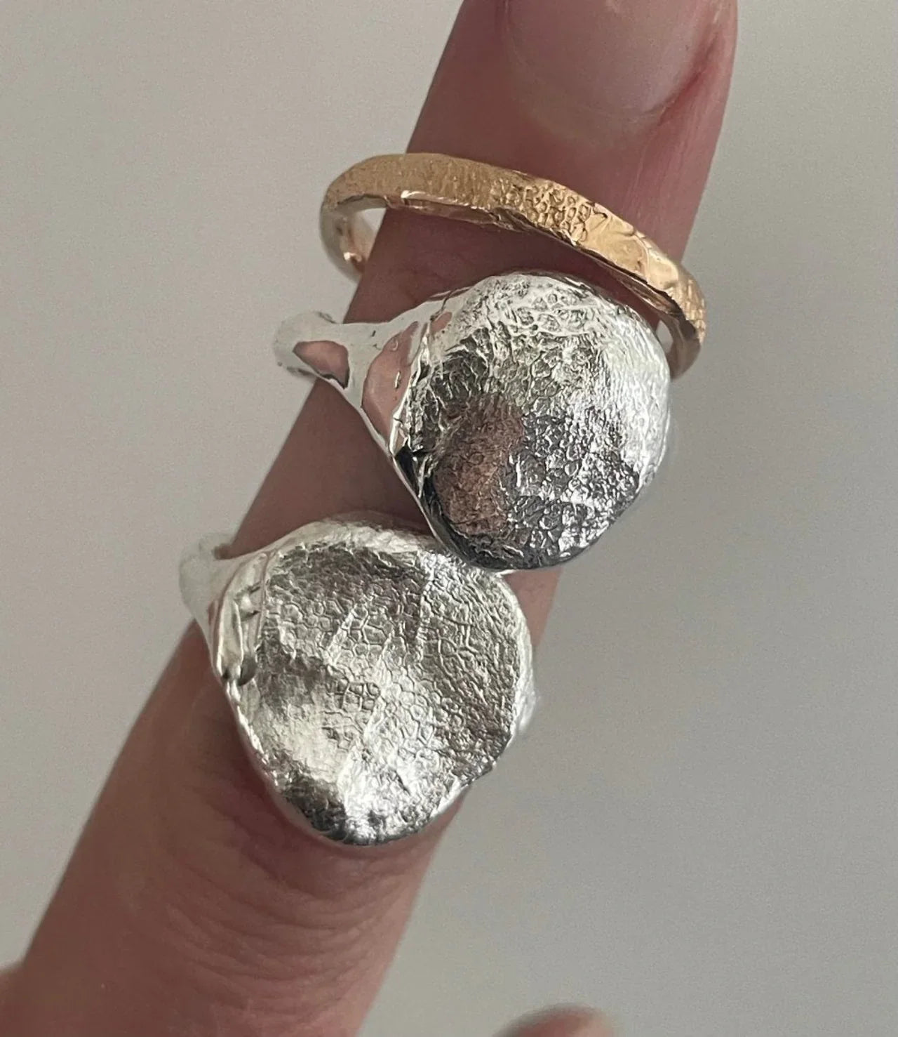 Close-up of three handcrafted silver and gold dog nose and paw impression rings stacked on a finger. Each ring captures a unique pet nose or paw print, symbolizing a meaningful keepsake crafted from recycled precious metals.