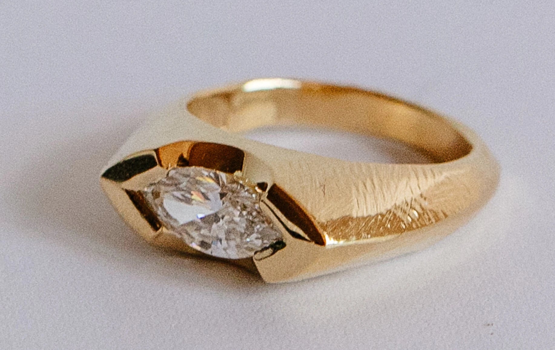 Gold wedding ring featuring an elegant diamond centerpiece, set against a soft neutral background.