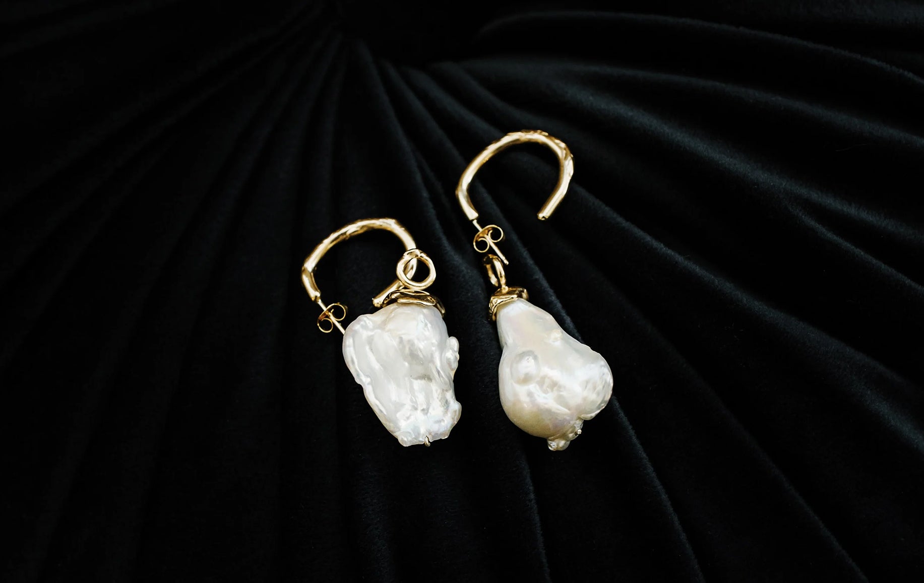 Gold pearl drop earrings featuring irregular baroque pearls, displayed elegantly on a rich black velvet background.