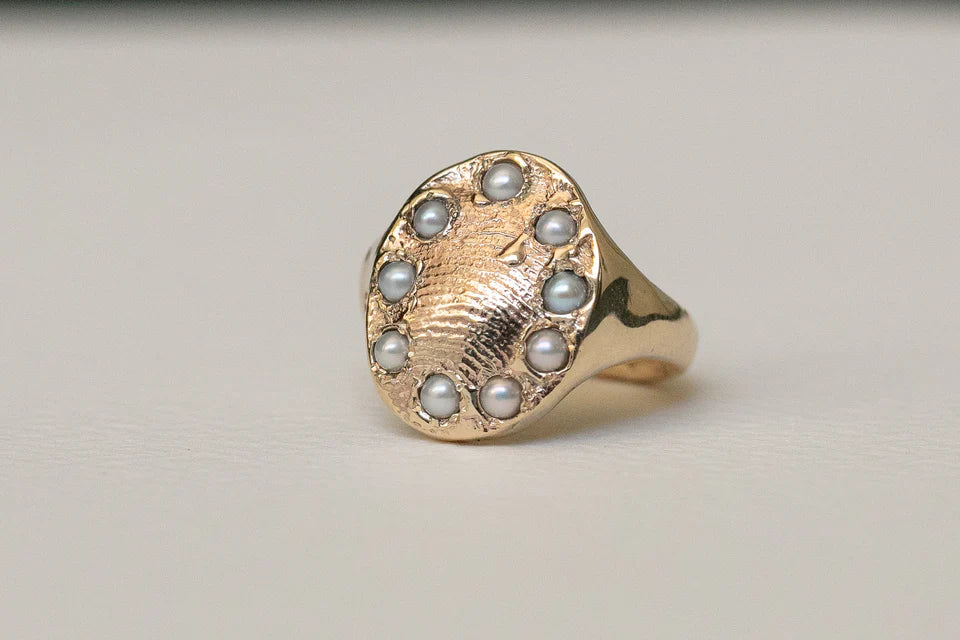 Gold ring featuring an intricate sunburst pattern with pearls delicately set in a circular arrangement.